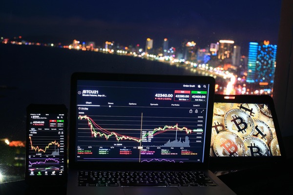 Cryptocurrency trading charts on a laptop and phone at night with a city skyline